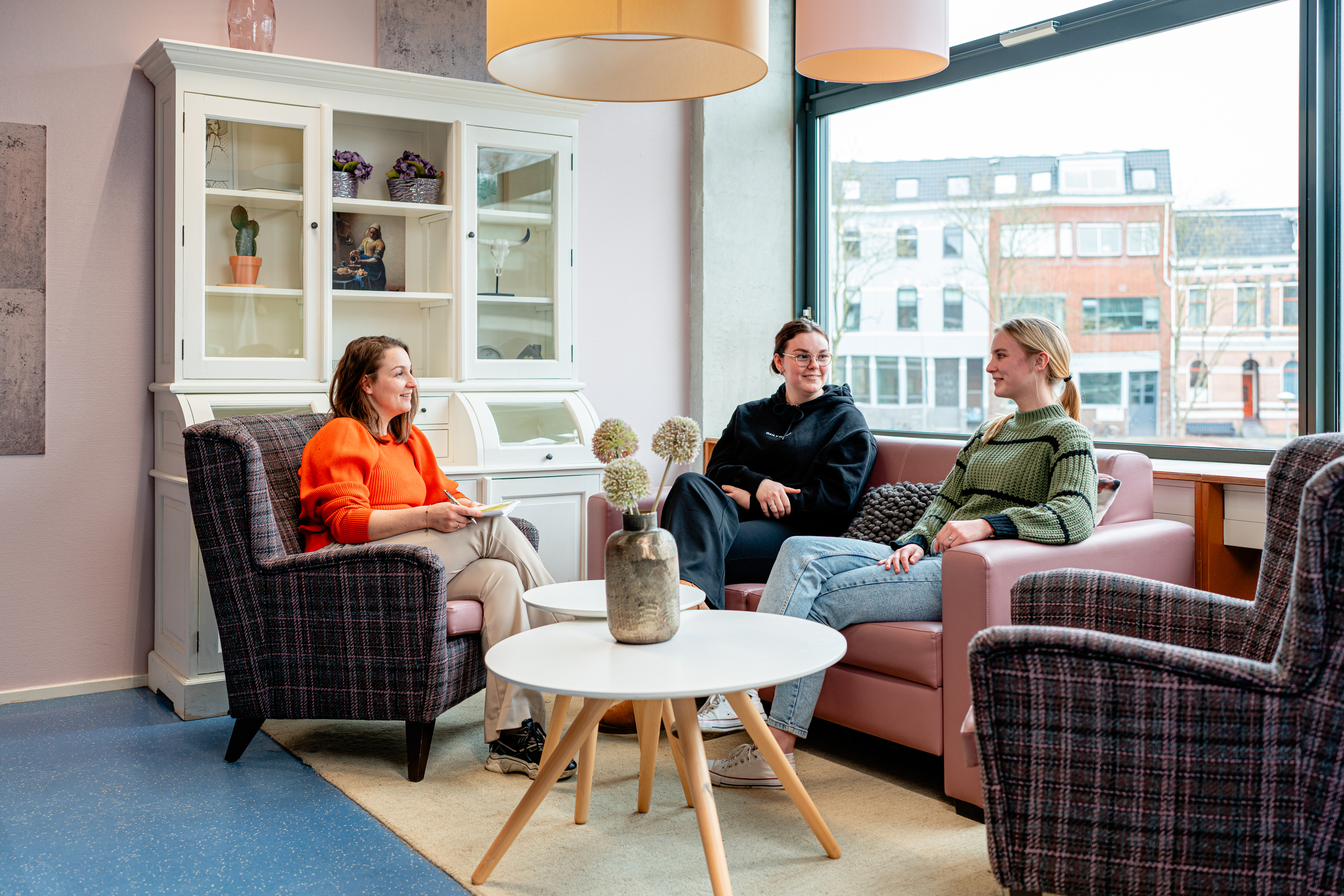 Drie personen in gesprek in een rustige gespreksruimte, passend bij maatschappelijke zorg en begeleiding.