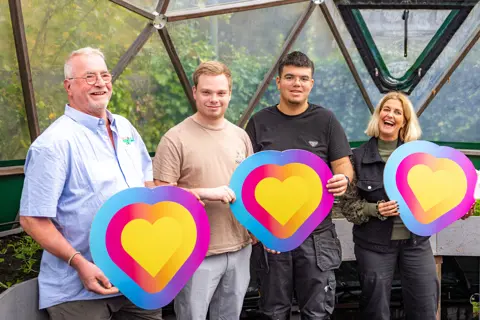 Vier betrokken personen bij De Dome Stadskanaal houden kleurrijke symbolen vast als teken van verbondenheid