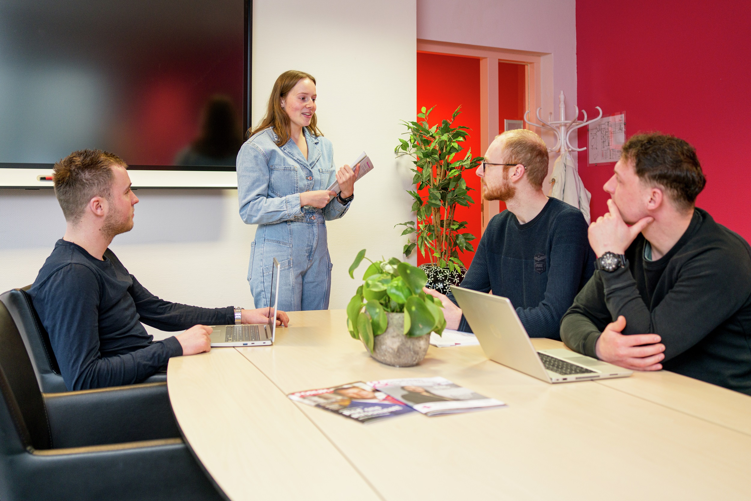 Een student geeft een presentatie aan een groep teamleden tijdens een overleg over leidinggevende taken.
