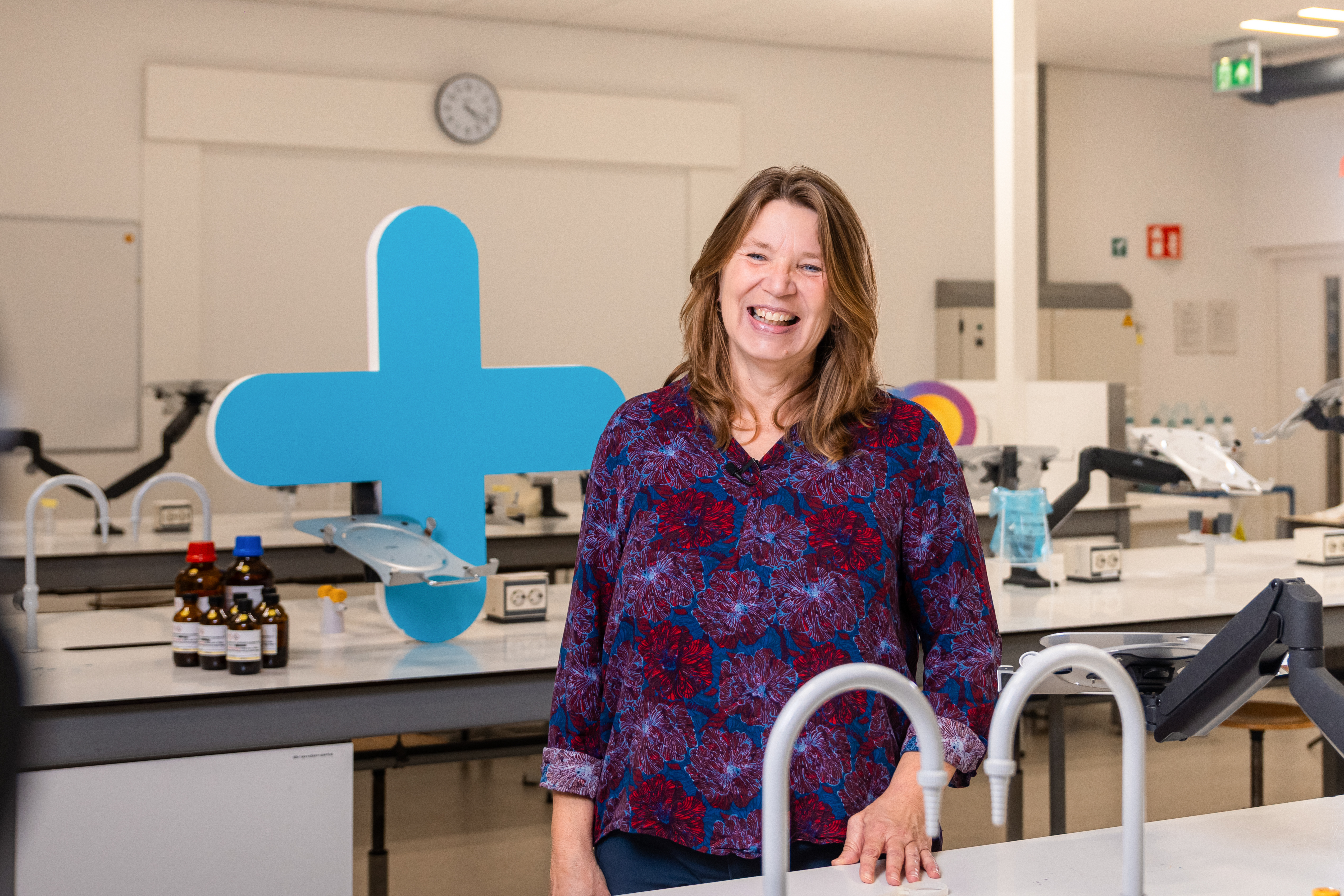 Docent in laboratoriumomgeving lacht trots, benadrukt betrokkenheid bij praktijkgericht technisch onderwijs