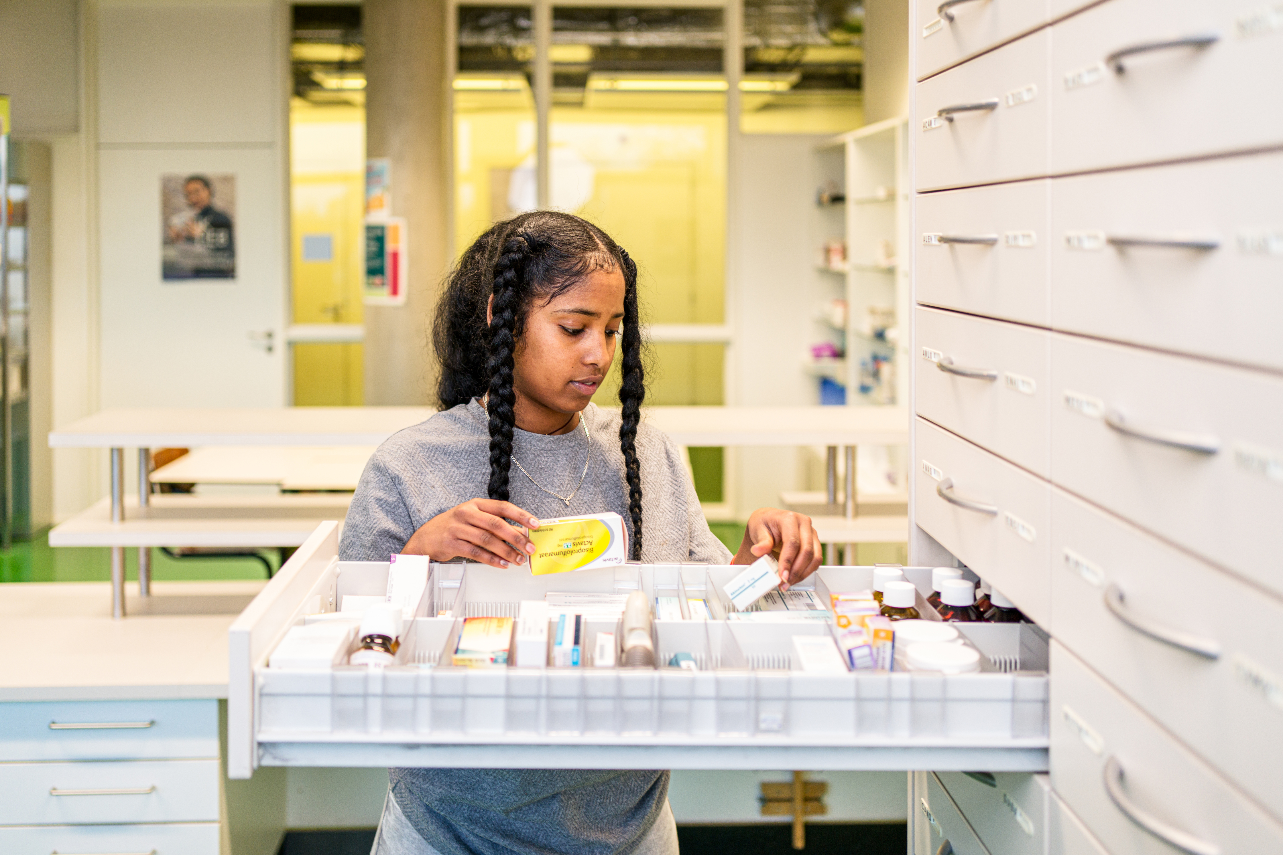 Student die medicatie en producten ordent in een apotheekkast tijdens een opleiding apothekersassistent
