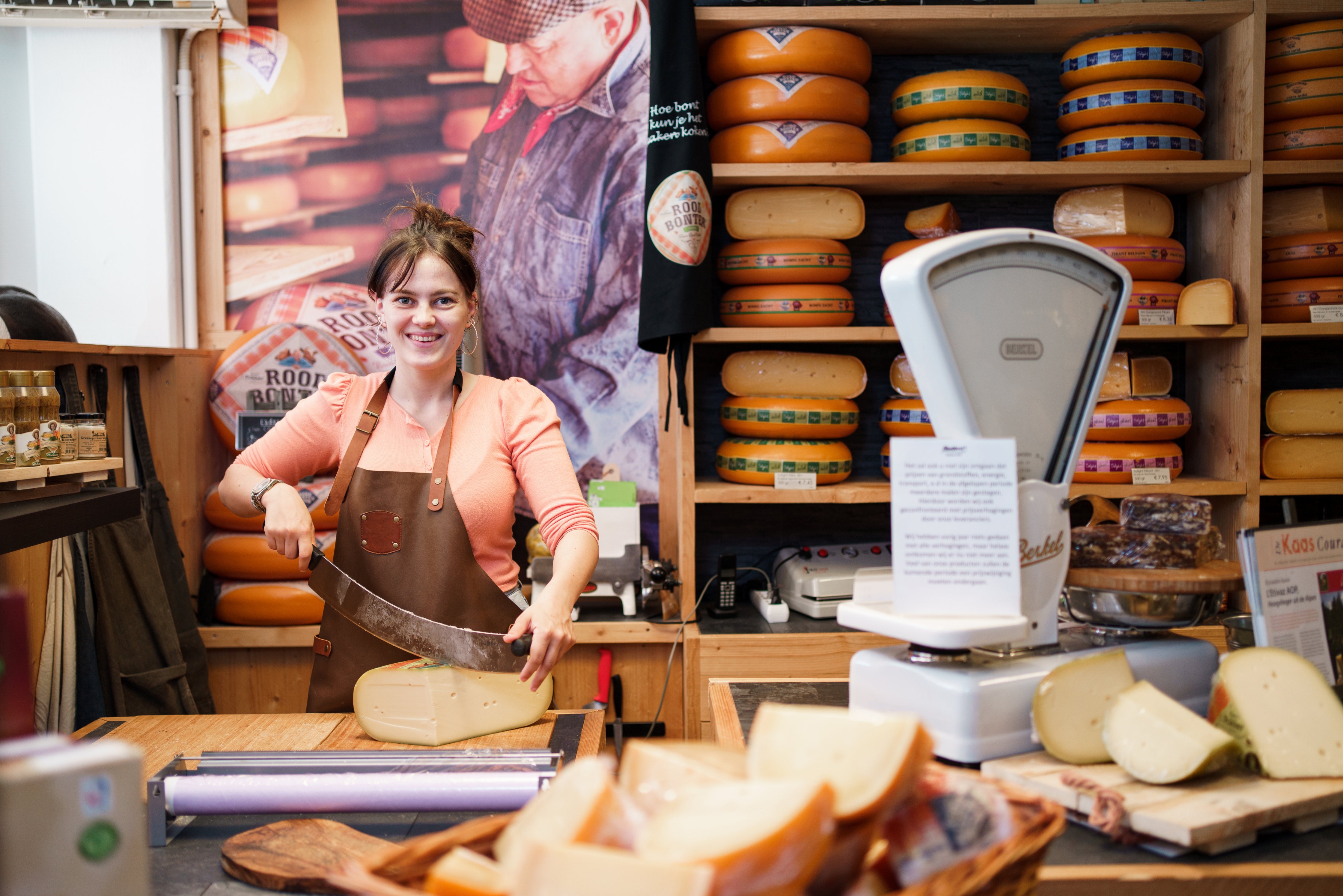 Medewerker snijdt kaas achter een toonbank in een retailomgeving met diverse kazen op voorraad