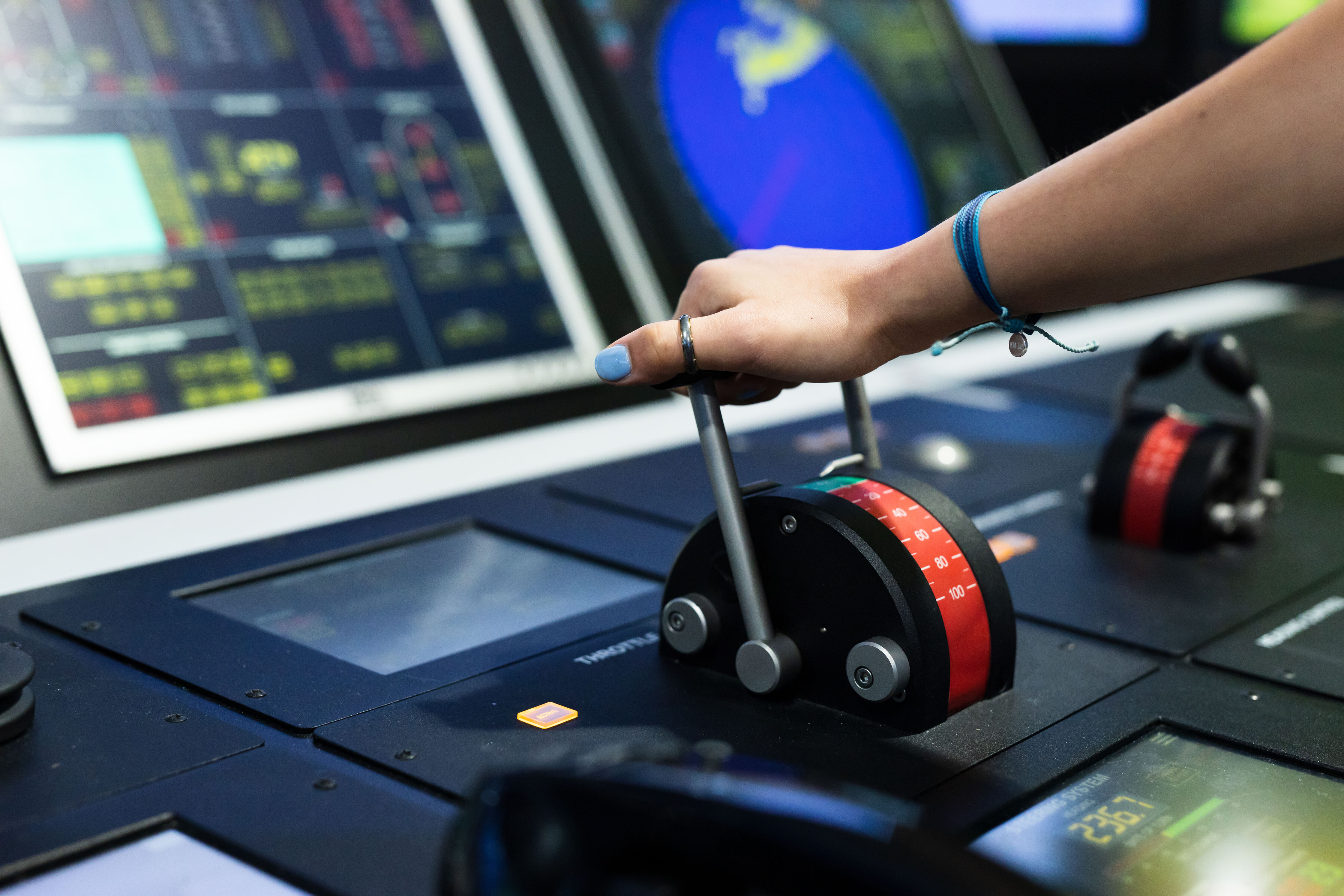 Hand bedient stuurhendels op brug van scheepssimulator met navigatieschermen op de achtergrond