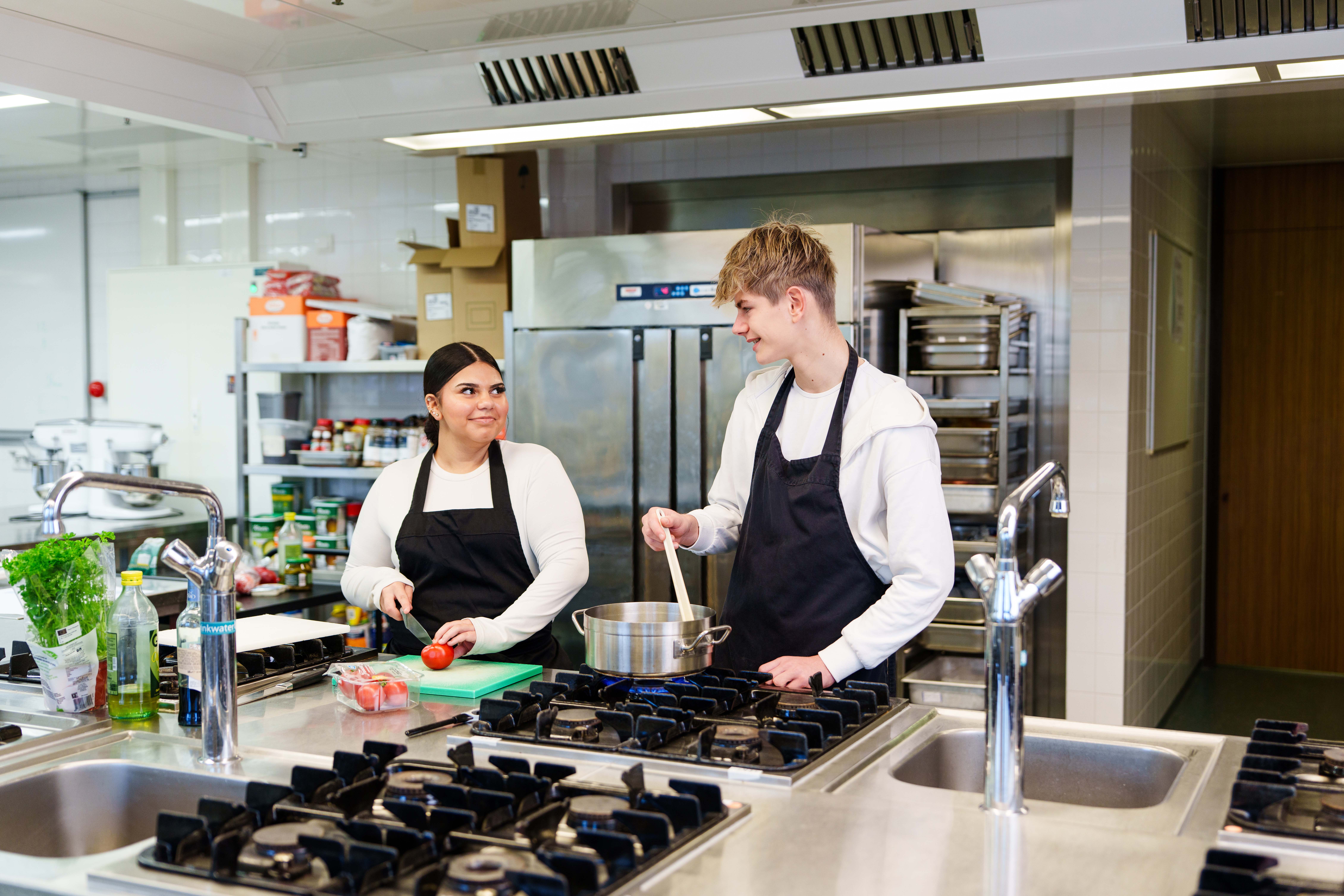 Twee studenten bereiden samen een maaltijd in een professionele keukenomgeving