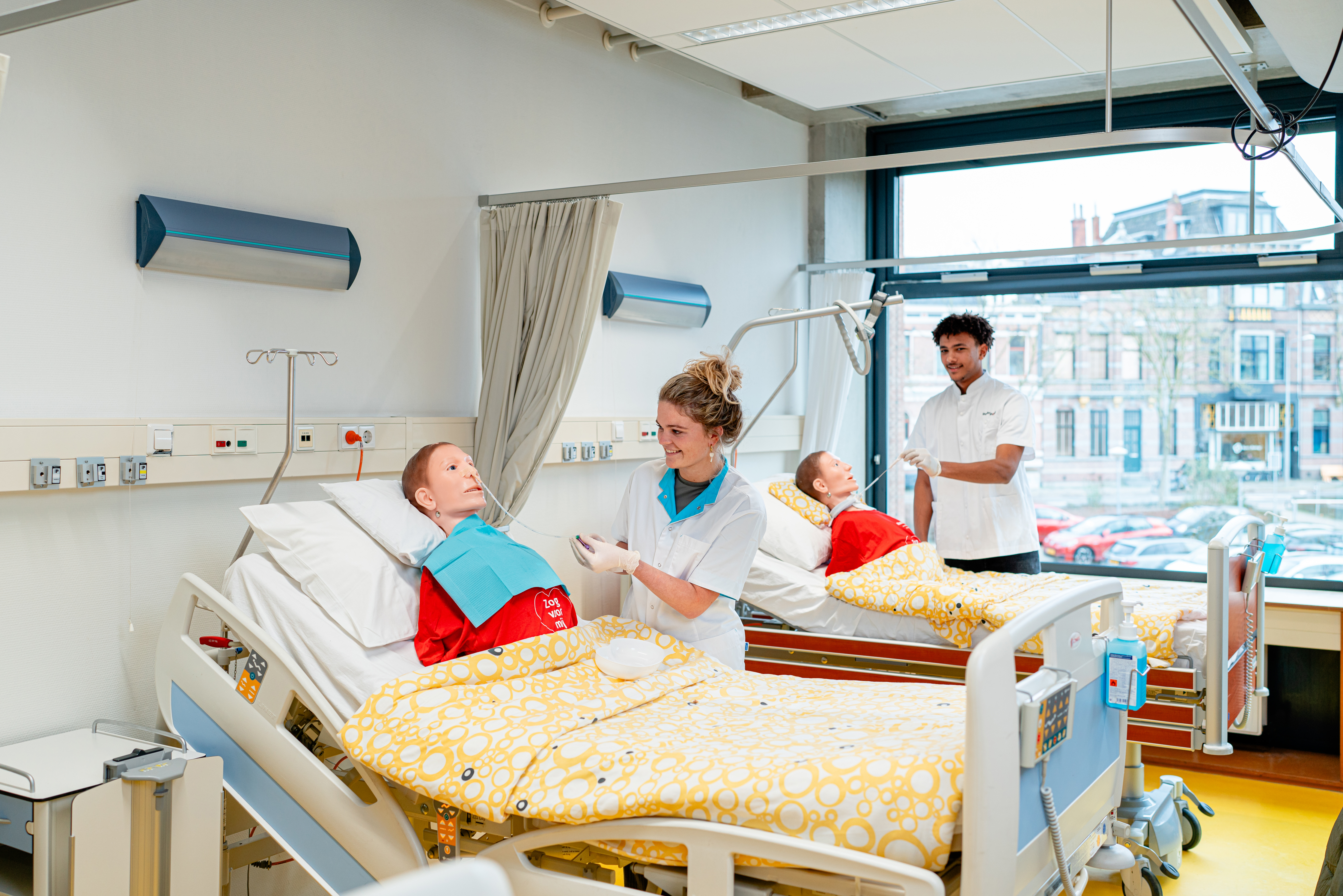 Studenten oefenen verpleegkundige handelingen waarbij een docent begeleiding biedt in een skillslabomgeving.