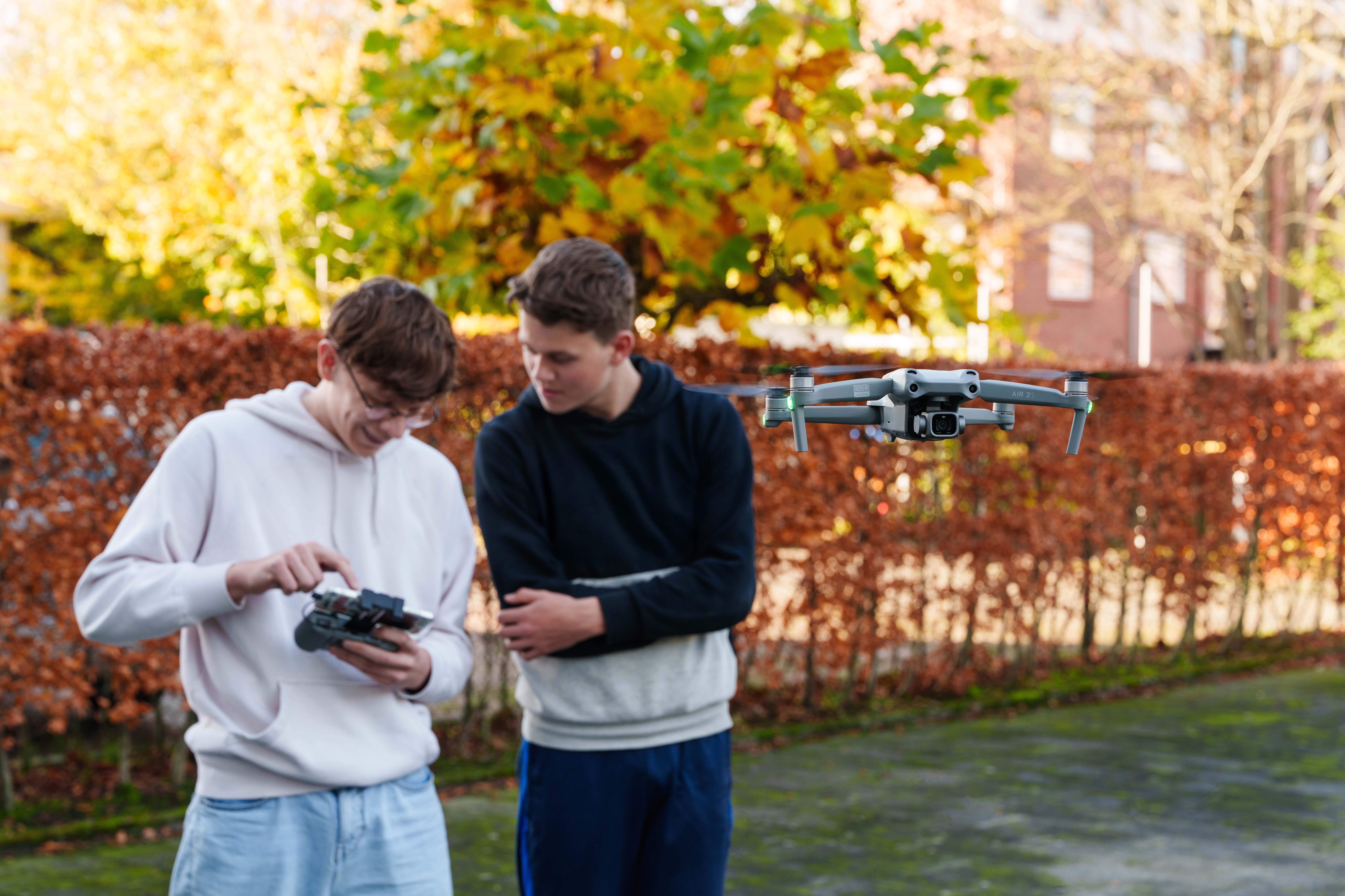 Twee studenten bedienen een drone met een afstandsbediening tijdens een praktijkles buiten
