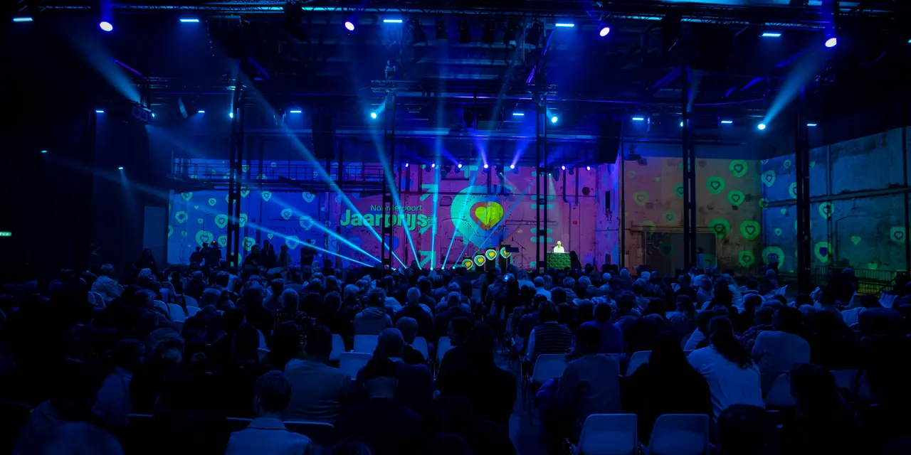 Publiek kijkt naar een podium met presentator tijdens de Noorderpoort Jaarprijs 2025 jubileumeditie.
