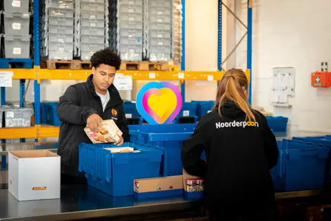 Logistiekstudenten sorteren en verpakken voedselpakketten in een magazijn voor maatschappelijke ondersteuning