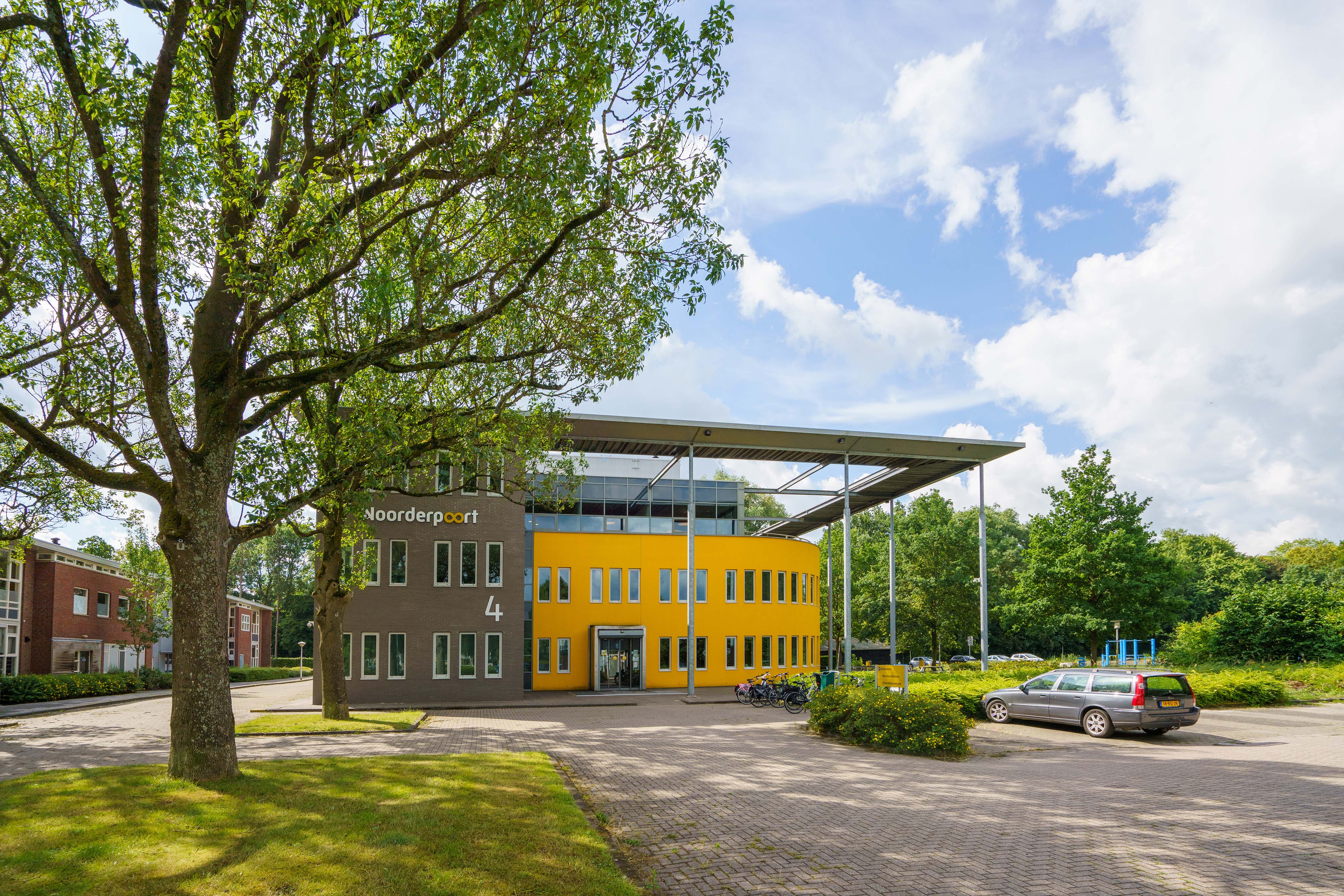 Gebouw van Noorderpoort bestuursbureau aan Verzetsstrijderslaan 4 in Groningen met parkeerterrein en bomen